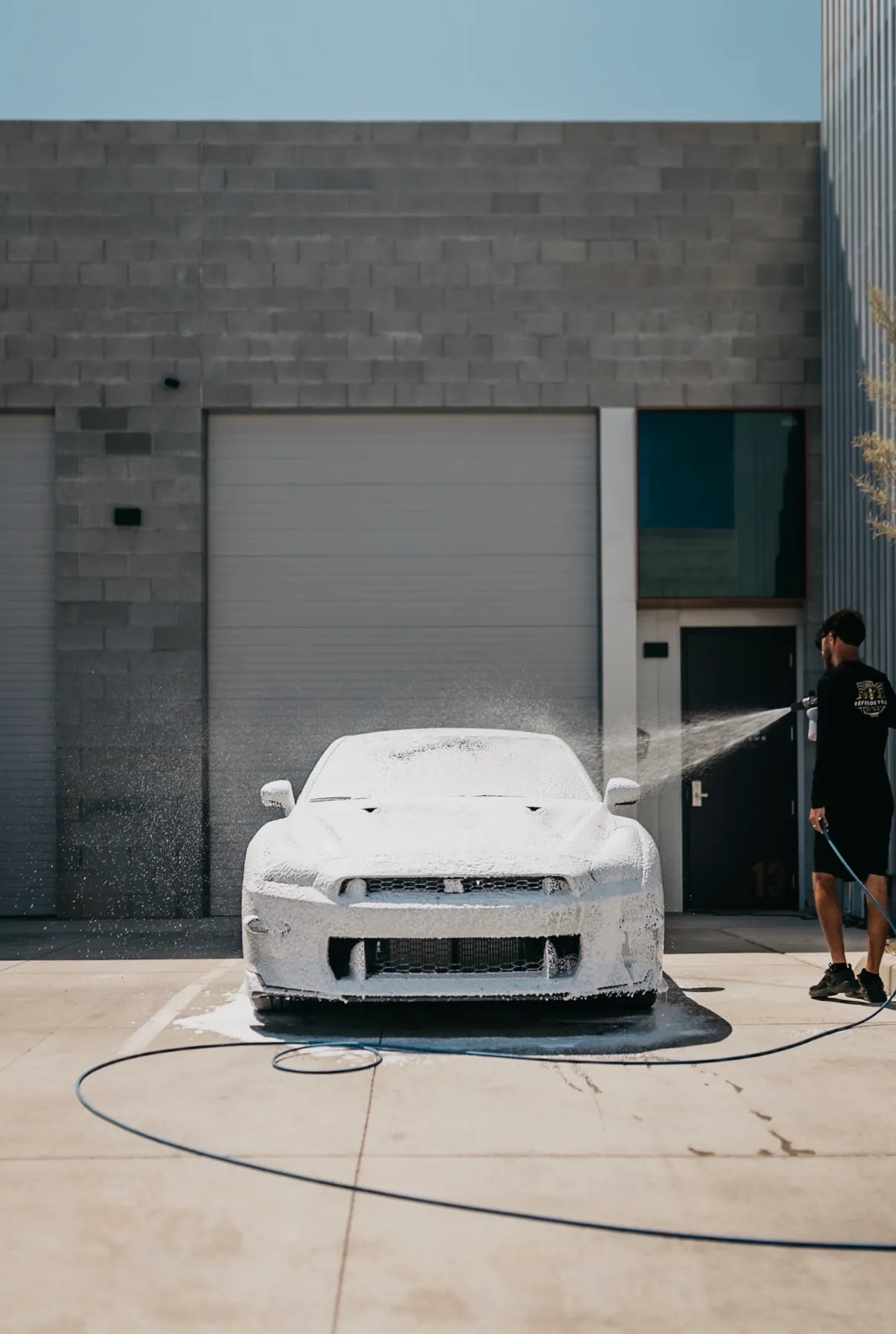 A Nissan GT-R covered in thick foam during a Reyes Details mobile wash, with the detailer rinsing from the side