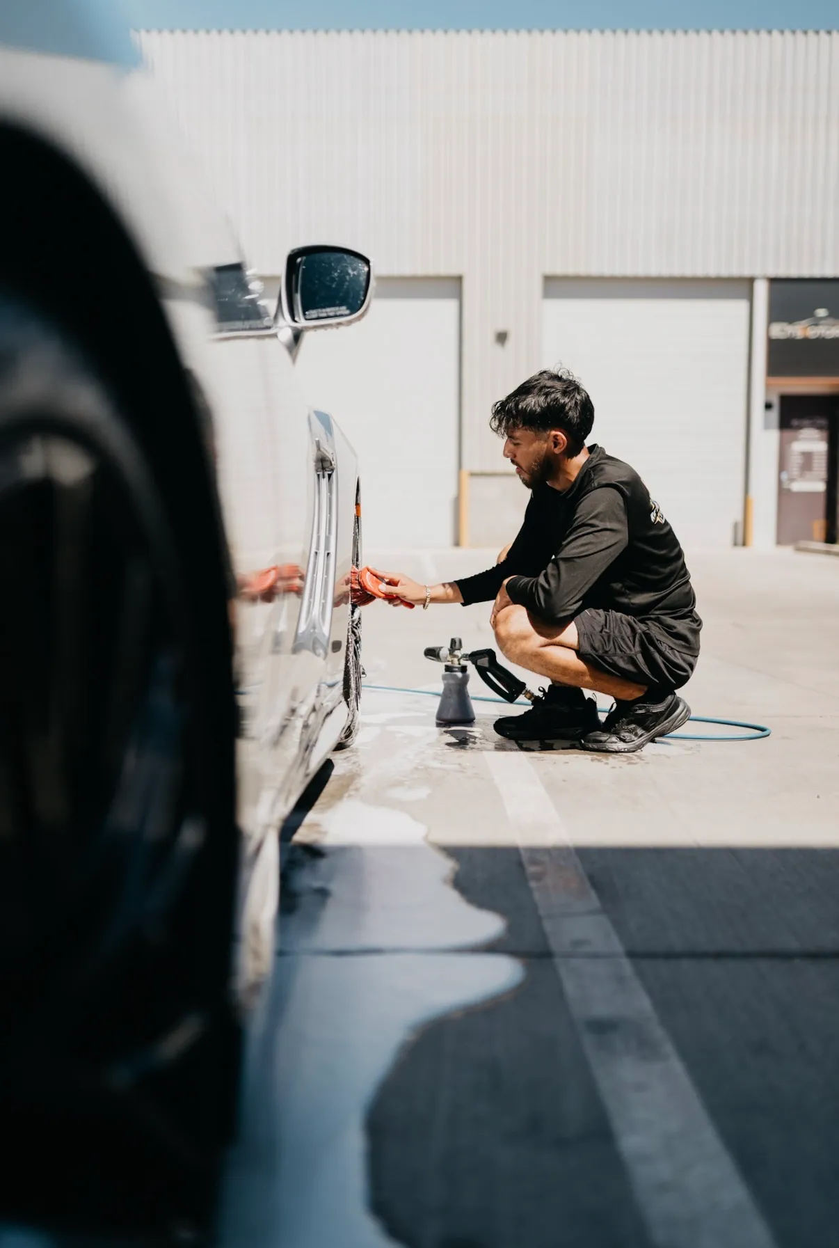 Reyes Details technician detailing the lower door and rocker panel of a white truck on a driveway
